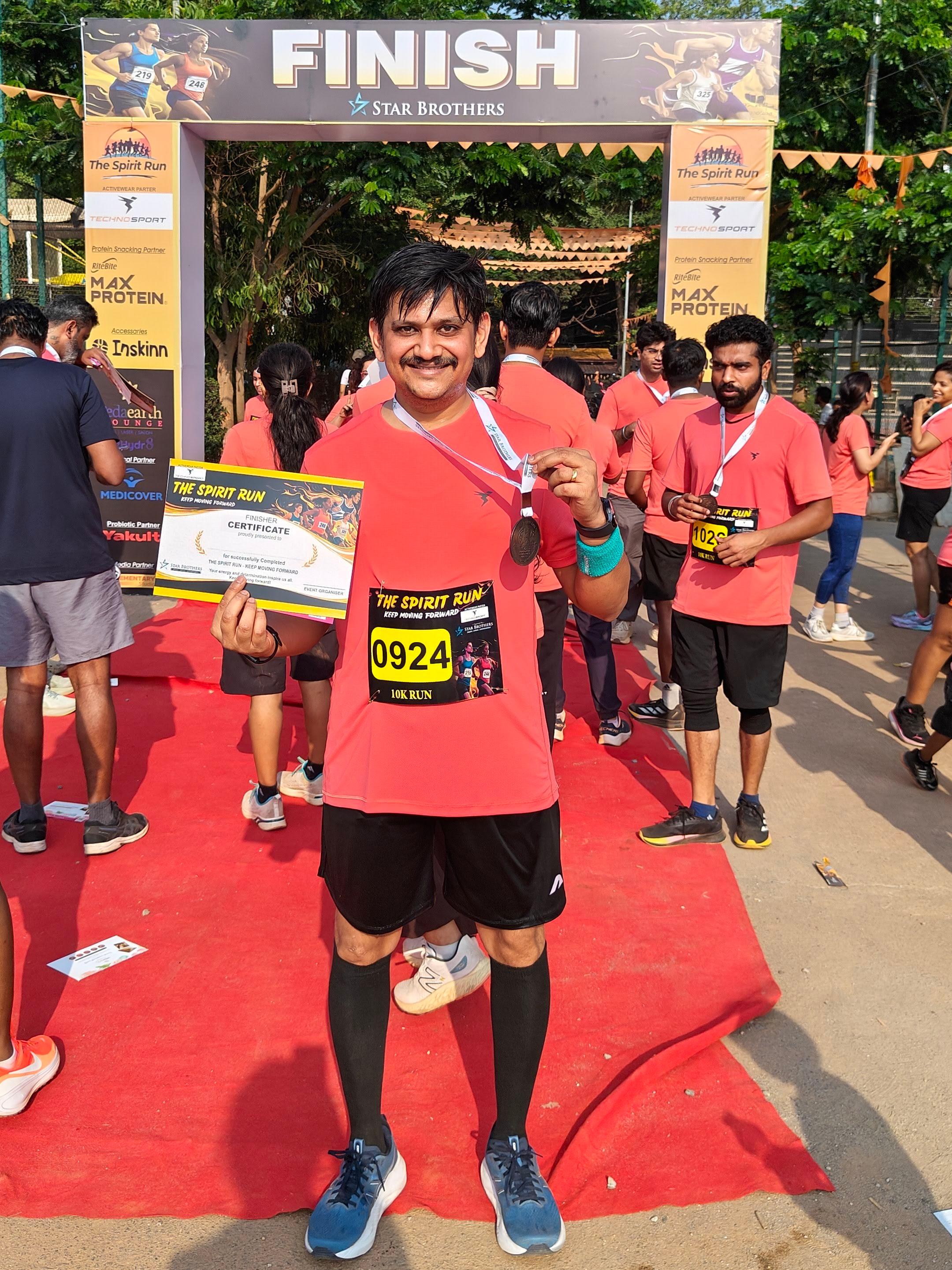 Akshay at the FINISH line of The Spirit Run 10k race holding finisher medal and certificate, April 19 2026